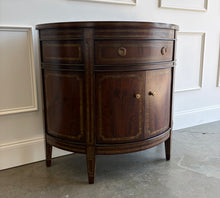 Load image into Gallery viewer, The Demilune Cabinet by Ambella Home combines graceful curves with richly figured wood veneer and classical detailing. Antiqued gold accents outline the drawer, doors, architectural panels, and tapered legs, emphasizing the cabinet’s rounded silhouette. A spacious upper drawer with decorative ring pulls provides convenient storage for smaller essentials, while two curved doors open to reveal an interior shelf for larger items. Good Bones Furniture