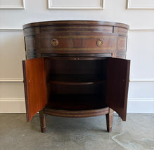 Load image into Gallery viewer, The Demilune Cabinet by Ambella Home combines graceful curves with richly figured wood veneer and classical detailing. Antiqued gold accents outline the drawer, doors, architectural panels, and tapered legs, emphasizing the cabinet’s rounded silhouette. A spacious upper drawer with decorative ring pulls provides convenient storage for smaller essentials, while two curved doors open to reveal an interior shelf for larger items. Good Bones Furniture