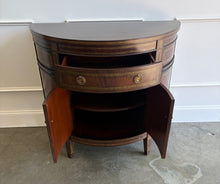 Load image into Gallery viewer, The Demilune Cabinet by Ambella Home combines graceful curves with richly figured wood veneer and classical detailing. Antiqued gold accents outline the drawer, doors, architectural panels, and tapered legs, emphasizing the cabinet’s rounded silhouette. A spacious upper drawer with decorative ring pulls provides convenient storage for smaller essentials, while two curved doors open to reveal an interior shelf for larger items. Good Bones Furniture