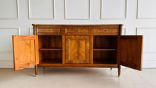 Load image into Gallery viewer, A study in balance and material, the Riley Sideboard draws from European neoclassical design—most notably Louis XVI—reimagined through a quieter, more modern lens. The form is clean and architectural, defined by symmetry, framed panels, and gently tapered legs that give the piece a sense of structure without excess. Cerejeira veneers are carefully bookmatched across each door, revealing a striking cathedral grain that brings movement and depth to the façade. Good Bones Furniture