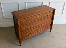 Load image into Gallery viewer, Gently used Ciborium chest by Sarreid showcases timeless European-inspired styling and exceptional craftsmanship. Constructed of solid walnut with a warm fruitwood finish, the piece features fluted corner columns, tapered turned legs, and three generously sized drawers accented with classic brass pulls and decorative faux keyhole escutcheons. Good Bones Furniture