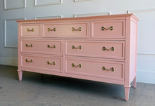 Load image into Gallery viewer, This vintage 7 drawer dresser by Drexel Furniture has been freshly lacquered in Benjamin Moore Mellow Coral, a warm blush-pink finish that gives the piece a soft, elevated look without losing its classic character. The clean rectangular case, framed drawer fronts, tapered legs, and original polished brass hardware create a tailored silhouette with subtle traditional detail. Good Bones Furniture