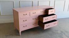 Load image into Gallery viewer, This vintage 7 drawer dresser by Drexel Furniture has been freshly lacquered in Benjamin Moore Mellow Coral, a warm blush-pink finish that gives the piece a soft, elevated look without losing its classic character. The clean rectangular case, framed drawer fronts, tapered legs, and original polished brass hardware create a tailored silhouette with subtle traditional detail. Good Bones Furniture