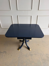 Load image into Gallery viewer, This Federal-inspired vintage drop-leaf table combines elegant classical details with space-saving versatility. Professionally lacquered in Benjamin Moore In the Navy, it features two rounded drop leaves, a single storage drawer with a decorative key and tassel, and a sculptural pedestal base finished with brass-capped feet. Good Bones Furniture