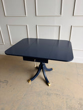 Load image into Gallery viewer, This Federal-inspired vintage drop-leaf table combines elegant classical details with space-saving versatility. Professionally lacquered in Benjamin Moore In the Navy, it features two rounded drop leaves, a single storage drawer with a decorative key and tassel, and a sculptural pedestal base finished with brass-capped feet. Good Bones Furniture