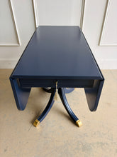 Load image into Gallery viewer, This Federal-inspired vintage drop-leaf table combines elegant classical details with space-saving versatility. Professionally lacquered in Benjamin Moore In the Navy, it features two rounded drop leaves, a single storage drawer with a decorative key and tassel, and a sculptural pedestal base finished with brass-capped feet. Good Bones Furniture