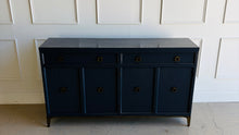 Load image into Gallery viewer, This like-new Hekman sideboard has been professionally refinished in a custom dark Sherwin Williams Naval lacquer, creating a rich, sophisticated finish that highlights the cabinet's clean lines and subtle oak grain texture. Antiqued brass hardware and a matching brass base add warmth and contrast, giving the piece a tailored, designer-inspired look. Good Bones Furniture