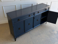 Load image into Gallery viewer, This like-new Hekman sideboard has been professionally refinished in a custom dark Sherwin Williams Naval lacquer, creating a rich, sophisticated finish that highlights the cabinet's clean lines and subtle oak grain texture. Antiqued brass hardware and a matching brass base add warmth and contrast, giving the piece a tailored, designer-inspired look. Good Bones Furniture