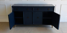Load image into Gallery viewer, This like-new Hekman sideboard has been professionally refinished in a custom dark Sherwin Williams Naval lacquer, creating a rich, sophisticated finish that highlights the cabinet's clean lines and subtle oak grain texture. Antiqued brass hardware and a matching brass base add warmth and contrast, giving the piece a tailored, designer-inspired look. Good Bones Furniture