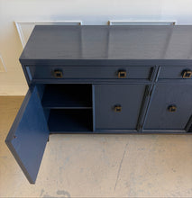 Load image into Gallery viewer, This like-new Hekman sideboard has been professionally refinished in a custom dark Sherwin Williams Naval lacquer, creating a rich, sophisticated finish that highlights the cabinet's clean lines and subtle oak grain texture. Antiqued brass hardware and a matching brass base add warmth and contrast, giving the piece a tailored, designer-inspired look. Good Bones Furniture