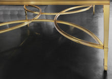 Load image into Gallery viewer, The Modern History Brielle Cocktail Table pairs clean lines with sculptural detail for a refined, airy centerpiece. Its polished brass frame is accented by an elegant stretcher in a flowing quatrefoil-inspired pattern that adds movement and visual interest beneath the glass top. The tempered clear glass surface keeps the silhouette light and open, allowing the brass framework to remain the focal point. Good Bones Furniture