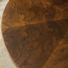 Load image into Gallery viewer, The Modern History Marchand End Table combines refined craftsmanship with sculptural design. A beautifully figured walnut veneer top showcases rich grain variation arranged in a radial pattern, giving the surface visual depth and warmth. The table’s elegant curved legs intersect with a brass stretcher, creating an architectural base that feels both light and structurally balanced. Good Bones Furniture