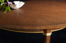 Load image into Gallery viewer, The Norris Dining Table by Modern History blends refined craftsmanship with understated glamour. Crafted in hand-rubbed walnut veneer, the table showcases a warm, richly toned surface that highlights the natural beauty of the wood grain. A sculptural apron accented with gold leaf detailing adds subtle luminosity beneath the tabletop, while slender tapered legs finished with brass ferrules provide an elegant finishing touch. Good Bones Furniture