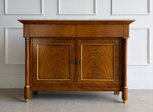 Load image into Gallery viewer, The Philippe Sideboard brings French Empire-inspired elegance and storage to a dining room, entryway, or living space. Crafted with richly figured cerejeira veneer, it features bookmatched door and drawer fronts, fluted columns, and hand-applied gold highlights. A polished white marble top creates a striking contrast with the warm wood tones. Two spacious drawers and a double-door cabinet with an interior shelf provide ample storage for serving pieces, linens, and other essentials. Good Bones Furniture