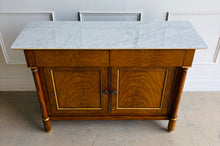 Load image into Gallery viewer, The Philippe Sideboard brings French Empire-inspired elegance and storage to a dining room, entryway, or living space. Crafted with richly figured cerejeira veneer, it features bookmatched door and drawer fronts, fluted columns, and hand-applied gold highlights. A polished white marble top creates a striking contrast with the warm wood tones. Two spacious drawers and a double-door cabinet with an interior shelf provide ample storage for serving pieces, linens, and other essentials. Good Bones Furniture