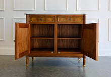 Load image into Gallery viewer, The Riley 2 Door Sideboard brings the graceful symmetry of European neoclassical design to a versatile, more compact scale. Crafted from mahogany solids with beautifully bookmatched cerejeira veneers, each door showcases a dramatic cathedral grain framed by hand-painted gold detailing. Two drawers keep smaller essentials close at hand, while the cabinet below provides generous concealed storage. Good Bones Furniture