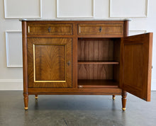 Load image into Gallery viewer, The Riley 2 Door Sideboard brings the graceful symmetry of European neoclassical design to a versatile, more compact scale. Crafted from mahogany solids with beautifully bookmatched cerejeira veneers, each door showcases a dramatic cathedral grain framed by hand-painted gold detailing. Two drawers keep smaller essentials close at hand, while the cabinet below provides generous concealed storage. Good Bones Furniture