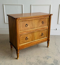 Load image into Gallery viewer, Elevate your bedside with the Riley Nightstand, a refined two-drawer piece that pairs timeless form with modern function. The front is clad in striking cerejeira veneer arranged in a radiant pattern and framed with hand-applied gold trim, while tapered legs finish with gilded caps for a subtle luxe note. Thoughtful scaling, warm mahogany tones, and elegant antique brass ring pulls make Riley an easy fit for both classic and contemporary bedrooms. Good Bones Furniture