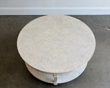 Load image into Gallery viewer, The Lucienne Cocktail Table by Theodore Alexander combines classical ornament with a light, graceful silhouette. Crafted from Khaya wood and richly figured Khaya swirl veneer, its round top rests above a fluted frieze accented with carved leaf motifs. Slender fluted legs connect the upper surface to a wide circular lower shelf. Washed Blanchette finish. Good Bones Furniture