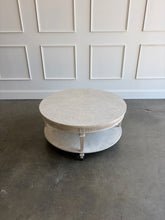 Load image into Gallery viewer, The Lucienne Cocktail Table by Theodore Alexander combines classical ornament with a light, graceful silhouette. Crafted from Khaya wood and richly figured Khaya swirl veneer, its round top rests above a fluted frieze accented with carved leaf motifs. Slender fluted legs connect the upper surface to a wide circular lower shelf. Washed Blanchette finish. Good Bones Furniture