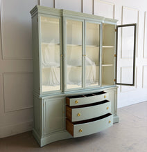 Load image into Gallery viewer, This vintage Bassett China Cabinet has been professionally lacquered in Benjamin Moore Saybrook Sage on the exterior with a creamy white interior for a bright, clean display. The classic silhouette features four glass doors on the upper hutch for showcasing china, glassware, and collections, while the lower cabinet offers a graceful serpentine front with ample closed storage. Warm brass knobs finish the look with an elegant, timeless contrast. Good Bones Furniture