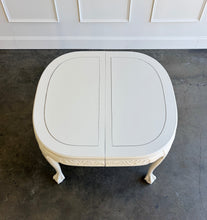 Load image into Gallery viewer, This vintage Chippendale-style dining table combines elaborate traditional detailing with a fresh, versatile finish. Professionally lacquered in Benjamin Moore Swiss Coffee darkened by 50%, it has a warm, creamy white appearance that highlights its carved details without feeling stark. Good Bones Furniture