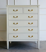 Load image into Gallery viewer, Vintage Dixie chest offers generous storage within a tall, space-conscious silhouette. Professionally lacquered in Benjamin Moore Swiss Coffee at 150% strength, its warm creamy-white finish complements the chest’s clean lines, inset drawer fronts, and tapered legs. Six drawers provide ample storage, while new solid brass drop-bail pulls add a polished contrast. Good Bones Furniture