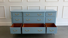 Load image into Gallery viewer, This vintage nine-drawer dresser by Ethan Allen combines generous storage with graceful traditional detailing. Professionally lacquered in a custom muted blue with soft gray undertones, the finish gives its classic silhouette a fresh, versatile look. Nine drawers provide abundant organized storage, while framed drawer fronts, a gently stepped top, curved apron, carved shell motif, and cabriole-style legs preserve its vintage character. Good Bones Furniture