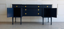 Load image into Gallery viewer, This vintage genuine mahogany sideboard combines generous storage with elegant Federal-inspired detailing. Professionally lacquered in Benjamin Moore In the Navy, its deep, classic navy finish highlights the fluted frieze, carved rosettes, decorative urn motifs, and slender tapered legs. New brass hardware. Good Bones Furniture