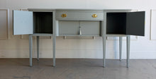 Load image into Gallery viewer, This vintage sideboard pairs a historic Hepplewhite-inspired silhouette with an unexpected modern color. Its gently bowed front, symmetrical layout, slender tapered legs, and balanced proportions reflect classic Federal design. Professionally lacquered in Sherwin-Williams Unusual Gray with new solid brass oval bail pulls with ornate neoclassical backplates. Good Bones Furniture