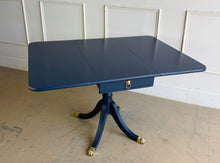 Load image into Gallery viewer, Classic Federal-inspired styling meets a fresh designer finish in this beautifully restored vintage drop leaf table. Professionally lacquered in Sherwin-Williams Naval, this versatile piece features two drop leaves that transform it from a slim console into a generous dining, game, or entry table in seconds. A single center drawer provides convenient storage, while the freshly painted lion head ring pull and polished brass claw feet add timeless elegance and character. Good Bones Furniture