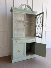Load image into Gallery viewer, This vintage china cabinet blends classic form with a fresh, tailored finish. Professionally lacquered in Benjamin Moore Saybrook Sage on the exterior and paired with a creamy white interior, it offers a soft contrast that brightens the display space and gives the piece a custom, updated feel. Arched fretwork glass doors and a sculptural pediment. Good Bones Furniture