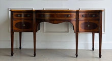 Load image into Gallery viewer, This vintage mahogany sideboard features graceful serpentine lines and exquisite satinwood inlay that highlight its timeless Federal-inspired design. The shaped top showcases a delicate inlaid urn motif, while bowed drawer fronts and paneled cabinet doors add depth and character throughout. A center drawer is flanked by two drawers above spacious side cabinets, providing generous storage for dining essentials or entertaining pieces. Good Bones Furniture