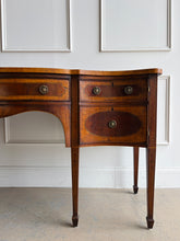 Load image into Gallery viewer, This vintage mahogany sideboard features graceful serpentine lines and exquisite satinwood inlay that highlight its timeless Federal-inspired design. The shaped top showcases a delicate inlaid urn motif, while bowed drawer fronts and paneled cabinet doors add depth and character throughout. A center drawer is flanked by two drawers above spacious side cabinets, providing generous storage for dining essentials or entertaining pieces. Good Bones Furniture