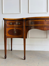 Load image into Gallery viewer, This vintage mahogany sideboard features graceful serpentine lines and exquisite satinwood inlay that highlight its timeless Federal-inspired design. The shaped top showcases a delicate inlaid urn motif, while bowed drawer fronts and paneled cabinet doors add depth and character throughout. A center drawer is flanked by two drawers above spacious side cabinets, providing generous storage for dining essentials or entertaining pieces. Good Bones Furniture