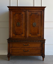 Load image into Gallery viewer, This vintage Mediterranean armoire has bold 1970s Spanish Revival styling with carved frieze detail, stepped door panels, burl veneer accents, and original brass ring hardware. The warm walnut-toned finish highlights the depth of the veneer, while the interior offers generous concealed storage with built-in drawers. Good Bones Furniture