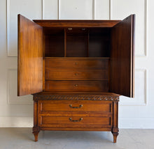 Load image into Gallery viewer, This vintage Mediterranean armoire has bold 1970s Spanish Revival styling with carved frieze detail, stepped door panels, burl veneer accents, and original brass ring hardware. The warm walnut-toned finish highlights the depth of the veneer, while the interior offers generous concealed storage with built-in drawers. Good Bones Furniture