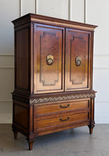 Load image into Gallery viewer, This vintage Mediterranean armoire has bold 1970s Spanish Revival styling with carved frieze detail, stepped door panels, burl veneer accents, and original brass ring hardware. The warm walnut-toned finish highlights the depth of the veneer, while the interior offers generous concealed storage with built-in drawers. Good Bones Furniture