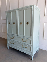 Load image into Gallery viewer, This vintage Thomasville armoire professionally lacquered in a custom muted green with soft blue-gray undertones, while the interior is finished in French Roast. Four paneled doors open to reveal divided upper compartments and two pull-out tray drawers. Two spacious lower drawers offer additional concealed storage. Good Bones Furniture