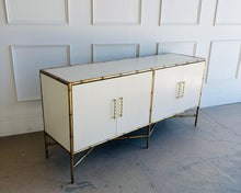 Load image into Gallery viewer, Angled view of the Ambella Home Chinoiserie Cabinet with linen finish panels, gold faux bamboo metal frame, and cross-stretcher bamboo-style base.