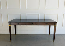 Load image into Gallery viewer, Front view hero image of the Theodore Alexander Bradbury Desk in Cambridge finish, crafted from khaya swirl wood with brass hardware, photographed at Good Bones Furniture in Raleigh, NC.