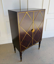 Load image into Gallery viewer, Angled right view of the Theodore Alexander Max bar cabinet with both doors closed, emphasizing the mahogany parquet door fronts, brass diamond trim, and sculptural silhouette.