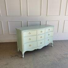 Load image into Gallery viewer, Angled view of a vintage French dresser featuring a soft green painted finish, curved silhouette, and brass ring pulls.