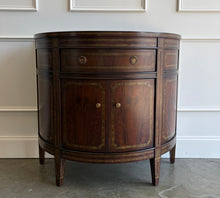 Load image into Gallery viewer, The Demilune Cabinet by Ambella Home combines graceful curves with richly figured wood veneer and classical detailing. Antiqued gold accents outline the drawer, doors, architectural panels, and tapered legs, emphasizing the cabinet’s rounded silhouette. A spacious upper drawer with decorative ring pulls provides convenient storage for smaller essentials, while two curved doors open to reveal an interior shelf for larger items. Good Bones Furniture
