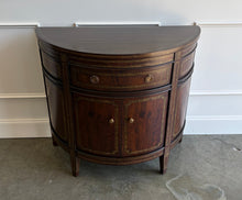 Load image into Gallery viewer, The Demilune Cabinet by Ambella Home combines graceful curves with richly figured wood veneer and classical detailing. Antiqued gold accents outline the drawer, doors, architectural panels, and tapered legs, emphasizing the cabinet’s rounded silhouette. A spacious upper drawer with decorative ring pulls provides convenient storage for smaller essentials, while two curved doors open to reveal an interior shelf for larger items. Good Bones Furniture
