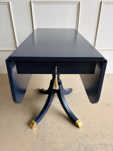 Load image into Gallery viewer, This Federal-inspired vintage drop-leaf table combines elegant classical details with space-saving versatility. Professionally lacquered in Benjamin Moore In the Navy, it features two rounded drop leaves, a single storage drawer with a decorative key and tassel, and a sculptural pedestal base finished with brass-capped feet. Good Bones Furniture
