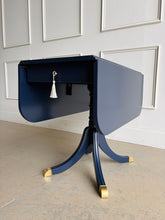 Load image into Gallery viewer, This Federal-inspired vintage drop-leaf table combines elegant classical details with space-saving versatility. Professionally lacquered in Benjamin Moore In the Navy, it features two rounded drop leaves, a single storage drawer with a decorative key and tassel, and a sculptural pedestal base finished with brass-capped feet. Good Bones Furniture
