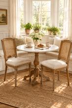 Load image into Gallery viewer, The Ellen Side Chair combines timeless European-inspired detailing with everyday durability. Crafted from solid mango wood, its distressed Beachwood finish highlights the carved frame, turned legs, and warm natural character of the wood. A handwoven cane back adds airy texture, while the upholstered seat is finished with classic nailhead trim. Sand Revolution Performance Fabric. Good Bones Furniture
