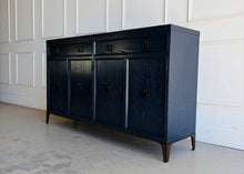 Load image into Gallery viewer, This like-new Hekman sideboard has been professionally refinished in a custom dark Sherwin Williams Naval lacquer, creating a rich, sophisticated finish that highlights the cabinet's clean lines and subtle oak grain texture. Antiqued brass hardware and a matching brass base add warmth and contrast, giving the piece a tailored, designer-inspired look. Good Bones Furniture
