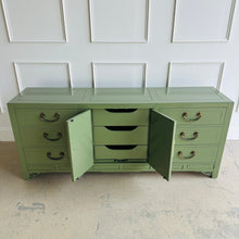 Load image into Gallery viewer, Green dresser with open doors against a white paneled wall.
